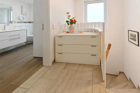 Flur mit Treppe und Kommode sowie Tageslicht.